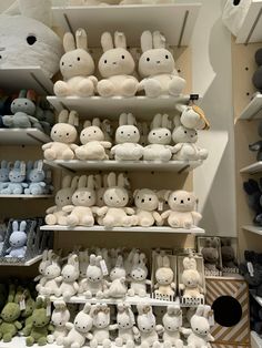 many stuffed animals are on shelves in a store with other items behind them, including one that is white and the other has black eyes