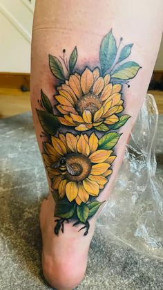 a sunflower tattoo on the leg with leaves and a bee sitting on top of it