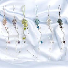 five different colored beads hanging from strings on a white sheet with satin material behind them