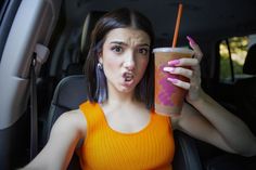 a woman in an orange top holding a drink and sticking her tongue out