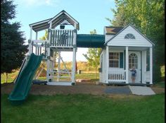 a small white house with a green slide next to it and a child's play area