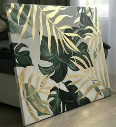 a large painting on the floor in front of a window with gold foiling and green leaves