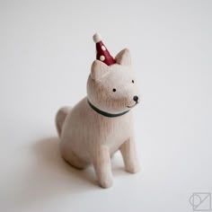 a small wooden toy dog with a red hat on its head and collar, standing in front of a white background