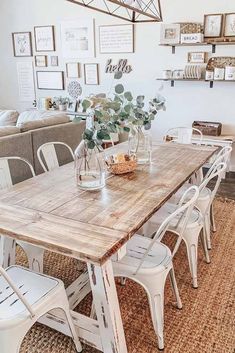 a wooden table surrounded by white chairs in a room with lots of pictures on the wall