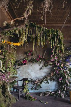 an arrangement of flowers and plants hanging from the ceiling in a room with concrete walls