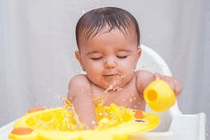 a baby sitting in a high chair playing with a yellow toy