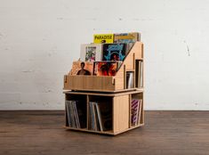 a book shelf with magazines and cds in it on a wooden floor next to a white brick wall