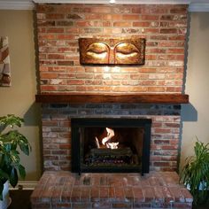 a brick fireplace in a living room with potted plants on the side and an art piece above it