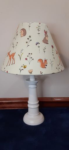 a lamp shade with animals and flowers on the lampshade, against a wall