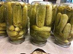 jars filled with pickles sitting on top of a table next to a piece of bread