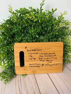 a wooden cutting board with writing on it next to some green plants and a potted plant