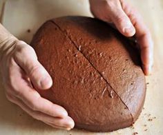 a person holding a large round cake on top of a wooden table next to a knife