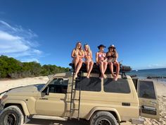 three women in bikinis sitting on top of a vehicle