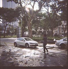 a person crossing the street in front of some cars on a rainy day with trees and buildings behind them