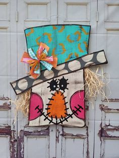 a scarecrow door hanger on the side of a wooden door with an orange bow