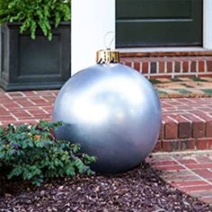 a large metal ball sitting on top of a garden bed next to a brick walkway