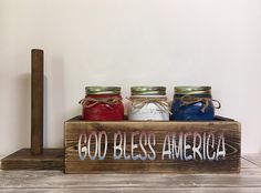 three jars are sitting on a wooden box with the words god bless america painted on it