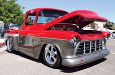 an old red truck is parked on the side of the road with its hood open