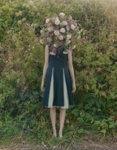 a woman standing in the grass with flowers on her head and hands behind her back