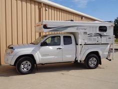 a white truck parked in front of a building with a camper on the back