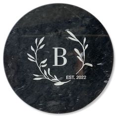 a black marble plaque with the letter b on it and an olive branch in the center