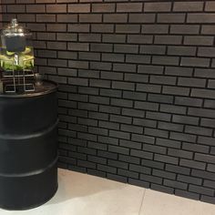 a large black barrel sitting in front of a brick wall next to a planter