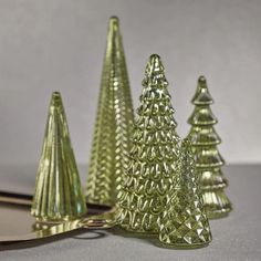 three green glass christmas trees sitting on top of a table next to a gold spoon