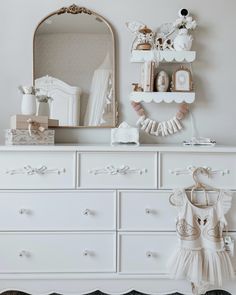 a white dresser topped with lots of drawers next to a mirror and wall mounted shelf