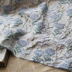 an open book on top of a table next to a blue and white flowered cloth