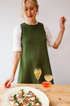 a woman standing in front of a plate of food on a table with two wine glasses