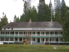 a large white building sitting in the middle of a lush green field next to tall trees