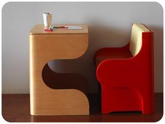 a red chair sitting next to a wooden table with a cup on top of it