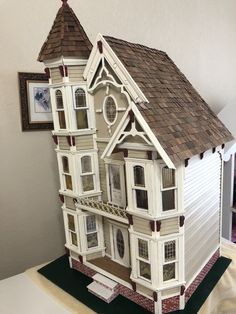 a doll house made out of wood and white with brown shingles on the roof