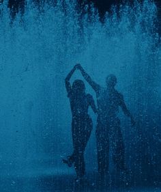 two people standing in front of a fountain with water splashing all around their bodies