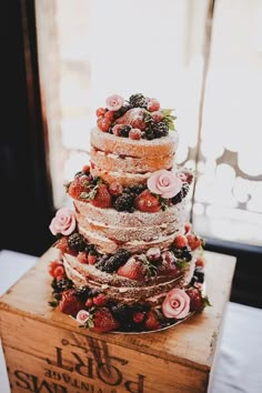 a three tiered cake with strawberries and roses on top is sitting on a wooden box