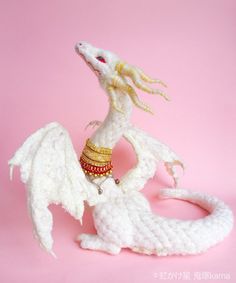 a white crocheted dragon figurine on a pink background