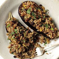 two stuffed eggplant halves on a white plate with a fork and spoon next to it