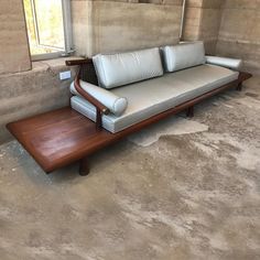 a couch sitting on top of a wooden table in front of a window with concrete walls