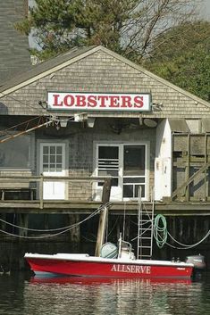 a red boat sitting in front of a lobsters restaurant on the water next to a dock