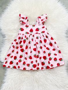 a pink strawberry print dress with red strawberries on it, sitting on a fluffy white rug