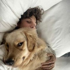 a woman laying in bed with her head on a large dog's back and eyes closed