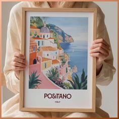 a woman holding up a framed poster with the words positano in front of her