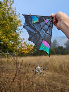 a hand holding a colorful spider kite in the middle of an open field with tall grass