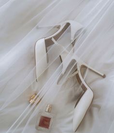 a pair of white high heeled shoes next to a perfume bottle on a bed