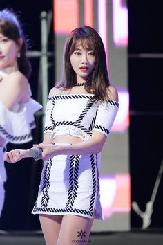 two women in white dresses standing on stage with one holding a microphone and the other wearing a black and white dress