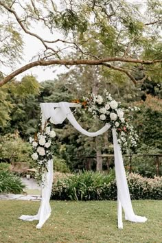 a wedding arch decorated with white flowers and greenery in the middle of a park