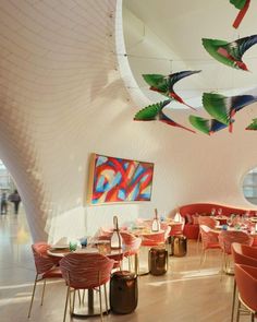 the interior of a restaurant with red chairs and colorful art hanging from the ceiling above