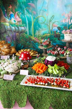 a table topped with lots of food covered in green grass next to a forest wall