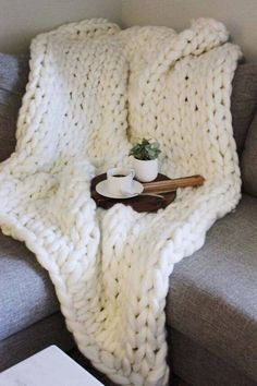 a white blanket sitting on top of a couch next to a cup and saucer