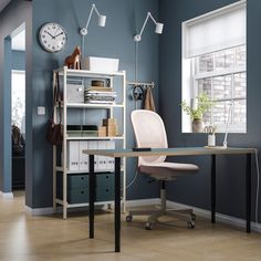 a desk with a laptop on it in front of a window and clock mounted to the wall